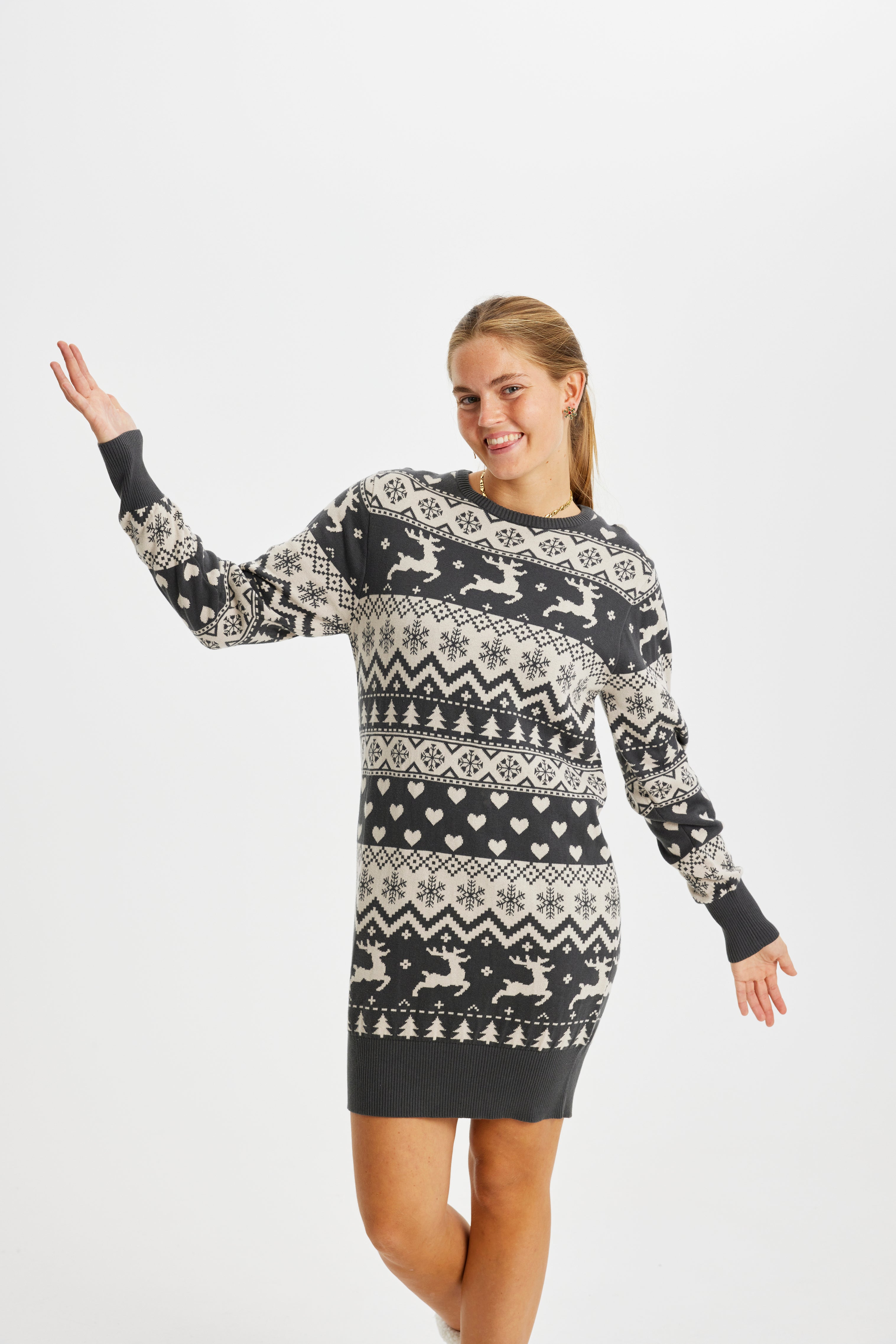 Une femme pose, vêtue d'une robe de Noël à rayures grises avec des rennes et un motif de Noël.